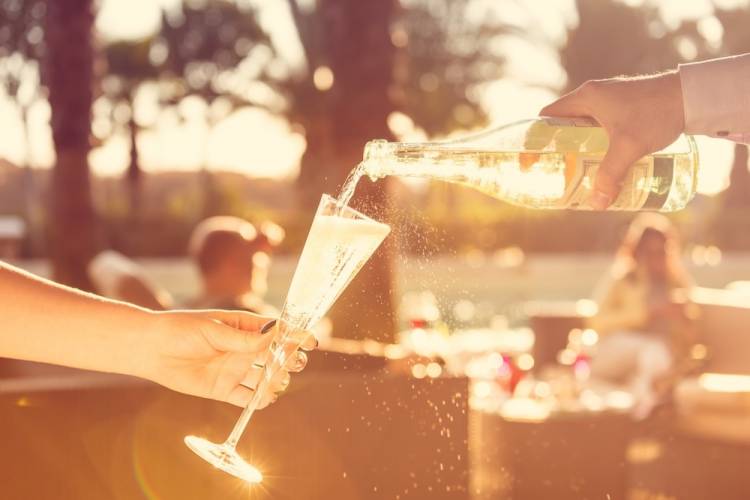 waiter pours champagne in glass outside on sunny day