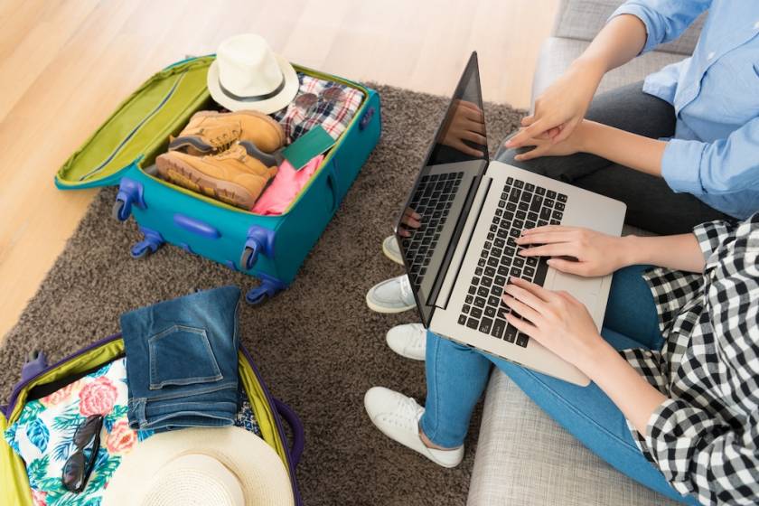 couple on computer looking for vacation destination. open suitcase beside them.