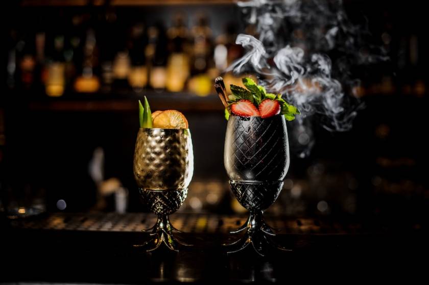 two cocktails in metal goblets on a bar